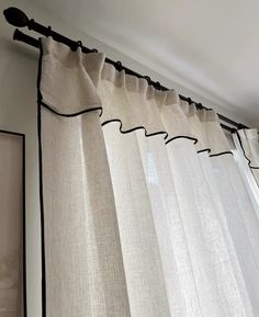 an open window with white curtains hanging from the side and black trimmings on the bottom