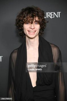 a woman with curly hair wearing a black dress and posing for the camera at an event