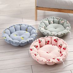 three pet beds on the floor in various colors and sizes, one with cherries