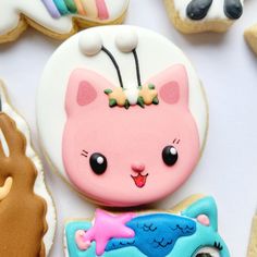 some decorated cookies are sitting on a white tablecloth and there is a pink cat in the middle