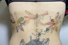 a woman's back with tattoos on her body and dragonflies in the background