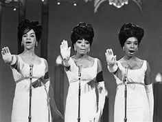 three women in white dresses standing next to each other with their hands up and singing into microphones