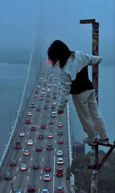 a person standing on the edge of a tall bridge with cars driving down it's sides