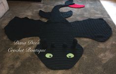 a crocheted black dragon laying on the floor with green eyes and tail, in front of a couch