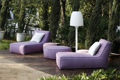 two purple lounge chairs sitting on top of a wooden deck next to plants and trees