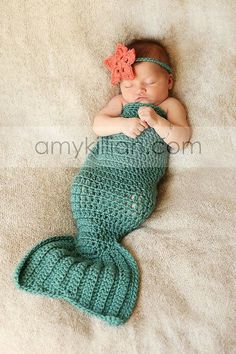 a baby sleeping on top of a blanket wearing a green mermaid tail with an orange flower in it's hair