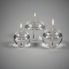 three clear glass candlesticks sitting next to each other on a white surface with one lit candle in the middle