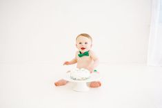 a baby sitting in front of a cake on top of a white plate and wearing a green bow tie