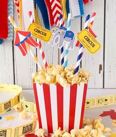 a red and white striped popcorn bucket with paper straws in it on a table