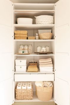 an organized pantry with baskets, towels and other items in white shelves on top of each shelf