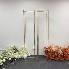 two tall gold metal plant stands in front of some white and orange flowers on the floor