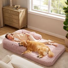 a woman laying on top of a pink bed next to a brown dog in a room