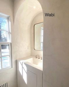 a bathroom with a sink, mirror and window next to it on the wall in front of an arched doorway