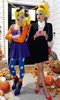 two women dressed in costumes standing next to each other with pumpkins on the ground