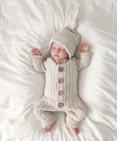 a baby wearing a knitted outfit and hat laying on top of a white blanket