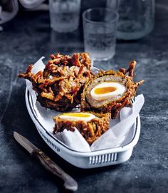 fried eggs and other food items in a basket on a table with utensils