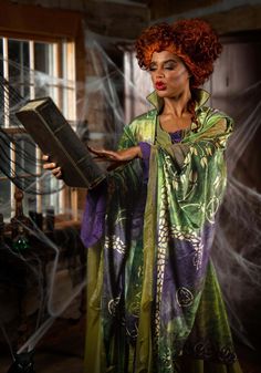 a woman with red hair is dressed in green and purple clothing while holding a book