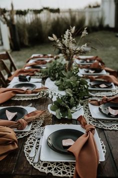 the table is set with black plates and brown napkins on it, along with greenery