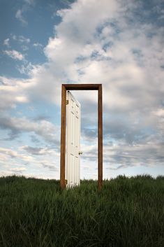 an open door sitting on top of a lush green field under a cloudy blue sky