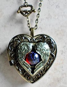 "Music box locket, heart locket with music box inside, in bronze with bronze filigree, angel wings and dragons breath opal cabochon. Heart music box pendant. This heart shaped music box is inspired by the gorgeous music box pendants of era's gone by. Music box is pill box size, please look at the dimensions for exact size. A heart shaped locket has been adorned with a layer of bronze heart shaped filigree with angel wings wrapped around a dragons breath opal cabochon in the center of the locket. Spiritual Antique Finish Jewelry Gift, Spiritual Antique Finish Jewelry, Spiritual Antique Finish Jewelry For Gift, Spiritual Antique Finish Jewelry As A Gift, Fantasy Brass Jewelry For Gifts, Red Antique Finish Jewelry Gift, Red Antique Finish Jewelry As Gift, Red Antique Finish Jewelry For Gift, Red Jewelry With Antique Finish As A Gift