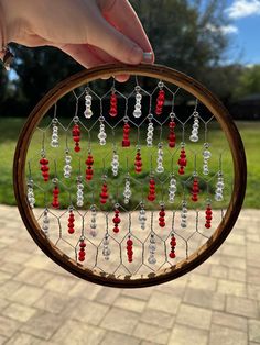 a hand holding a circular beaded frame with red and white beads hanging from it