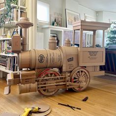 a cardboard model of a steam engine on the floor next to tools and bookshelves