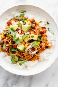 a white bowl filled with rice, beans and avocado on top of a marble table