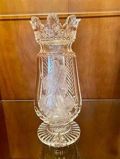 a glass vase with a statue in the center on a table top next to a wood paneled wall