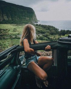 a woman is sitting in the back of a truck looking out at the ocean and mountains