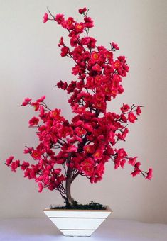 a bonsai tree with red flowers in a white bowl on a table top,