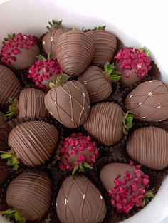 a white bowl filled with lots of chocolate covered strawberries and pink flowers on top