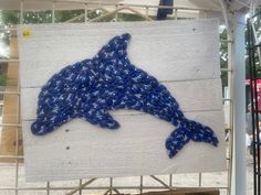 a blue dolphin made out of plastic bottles on a white board with people looking at it