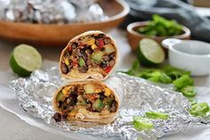 two burritos are stacked on top of each other in tin foil with vegetables