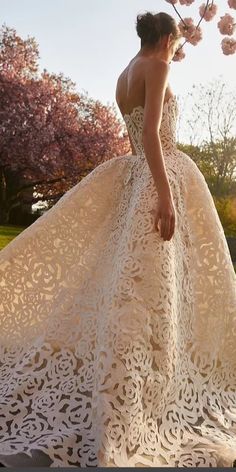 a woman in a white wedding dress standing next to a tree with pink flowers on it