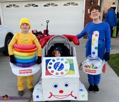 two children in costumes standing next to a toy car