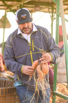 a man standing next to a wooden barrel holding up some rooty vegetables in his hands