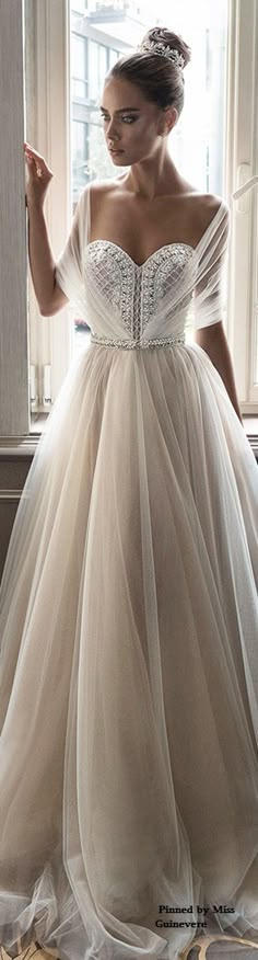 a woman in a wedding dress standing by a window with her hand on her hip