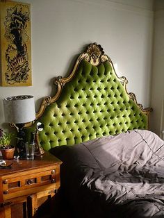 a bed with a green headboard sitting next to a lamp on a wooden table