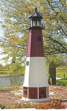 a red and white light house sitting in the middle of a park next to a tree