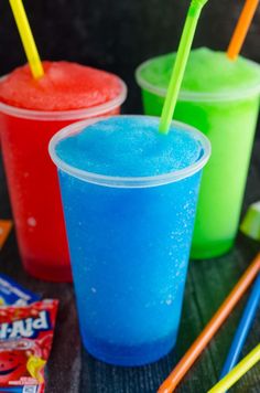 three different colored drinks with straws and candy bars in the background on a table