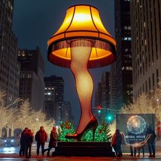 people are standing in front of a lighted lamp on a city street with tall buildings