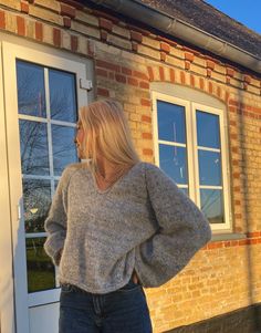 a woman standing in front of a brick building with her back to the camera, wearing jeans and a sweater