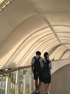 two people are standing on a walkway under a white structure with curved walls and metal railings