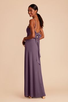 a woman in a long purple dress with a bow on the back, looking at something off to the side