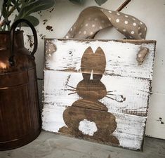 a wooden sign with a bunny on it next to a vase and potted plant