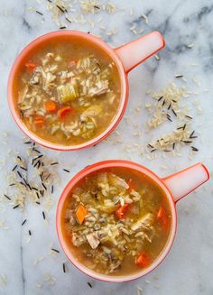 two orange mugs filled with soup on top of a marble counter next to oats