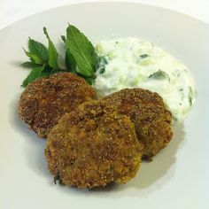 two crab cakes on a white plate with cream cheese and green leaves next to it