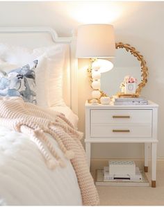 a bedroom with a white bed and a mirror on the nightstand next to it,