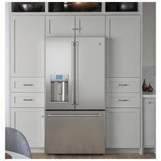 a stainless steel refrigerator in a kitchen with white cabinetry and drawers on either side