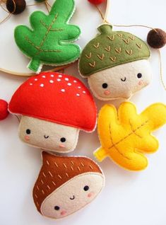 three felt mushrooms are hanging from a hoop on a white surface with red, green and yellow leaves